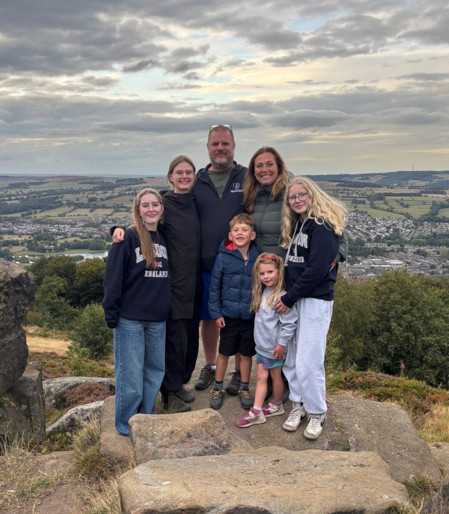 Happy family posing for photograph standing on rocks with a beautiful English landscape behind them