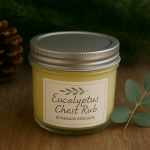 yellow homemade chest rub in clear glass jar with silver metal lid on a wood countertop with pinecone and eucalyptus sprig beside it. Healthy budget-friendly Christmas gifts – DIY chest rub.