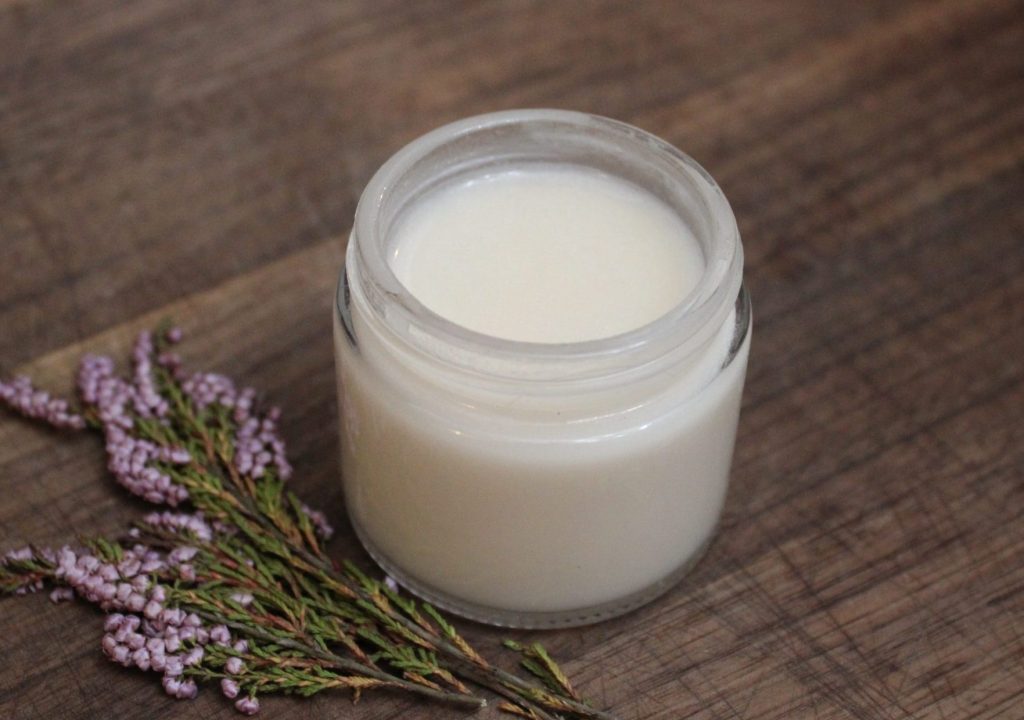 Jar on homemade natural deodorant sitting on top of a dark wood cutting board with dried flowers