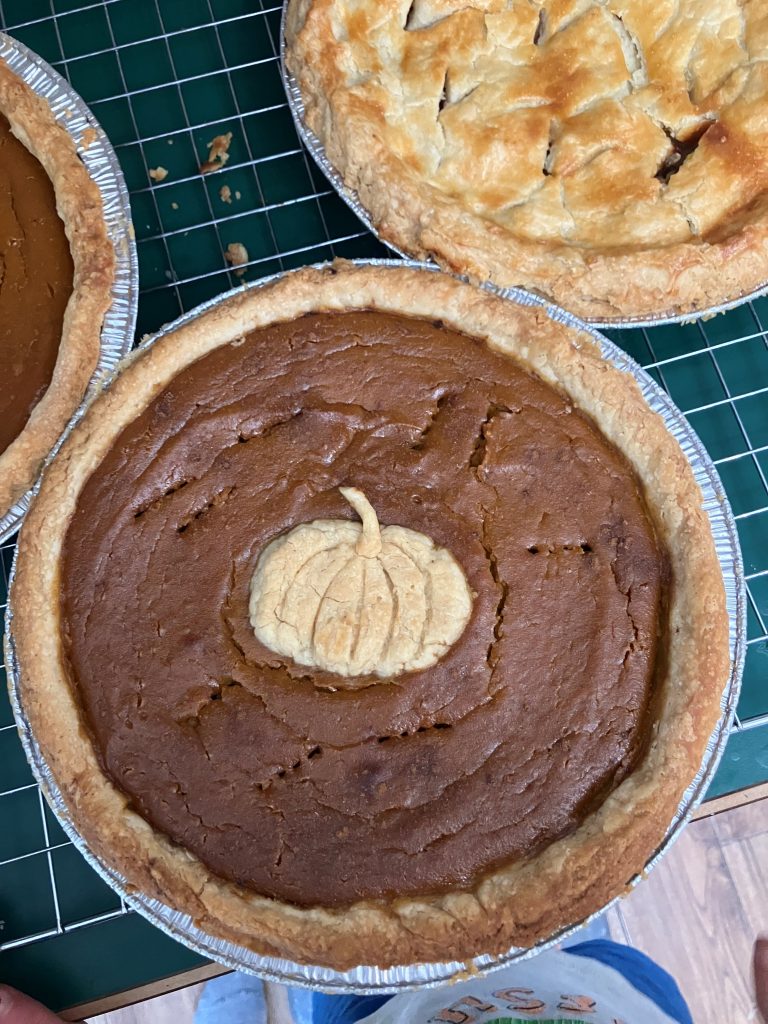 Freshly baked pumpkin pie with pumpkin shaped pastry cut out on center sitting on cooling rack
