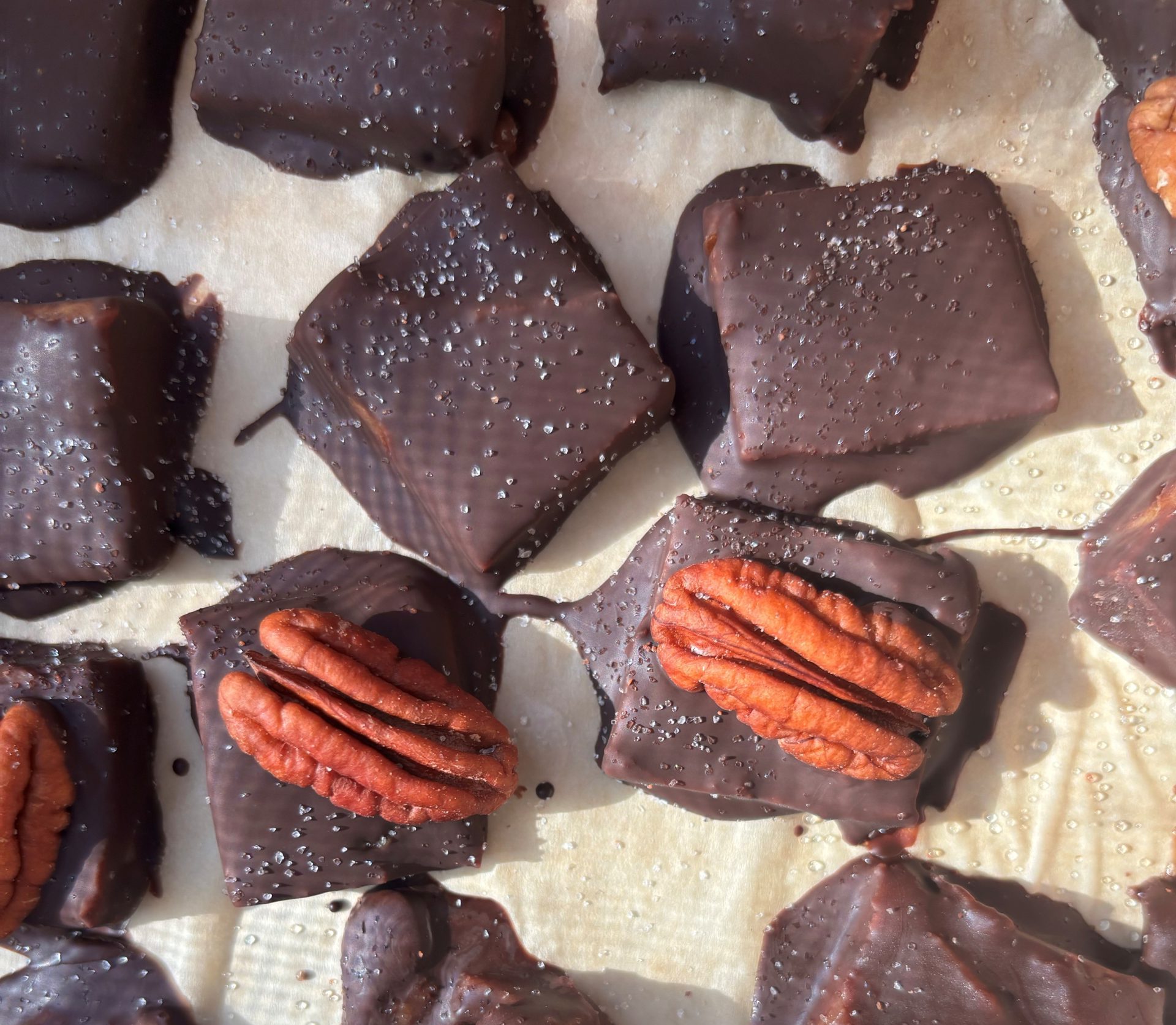 Close up of homemade Healthier Chocolate covered salted "caramels" made with dates. Some have pecans on top of them and all have sea salt.