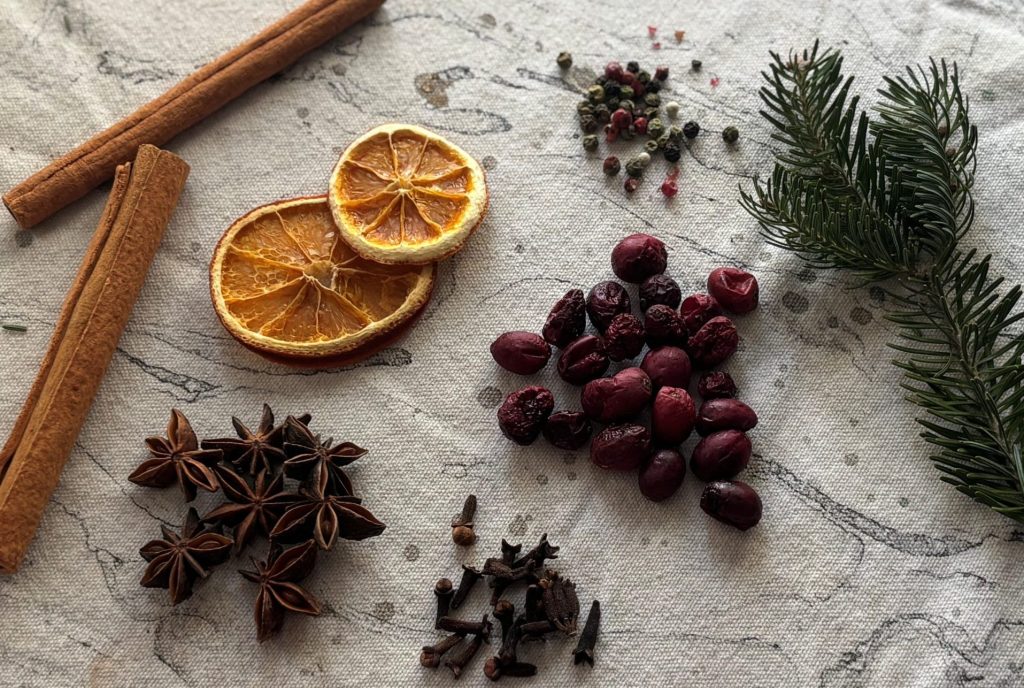 Cinnamon Sticks, dried orange slices, tri-colour peppercorns, star anise pods, dried cloves, dried cranberries, dried pine on neutral table cloth