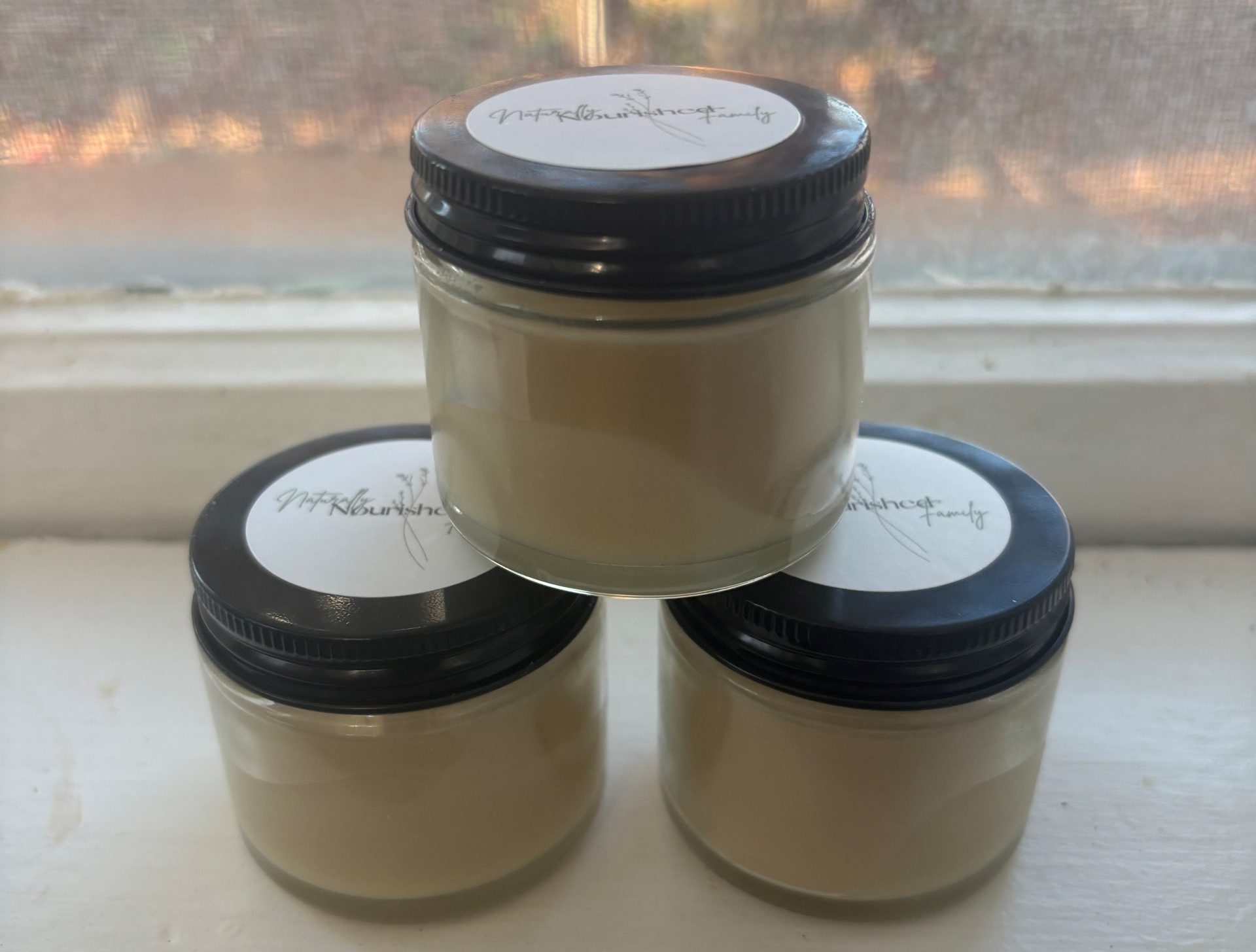 Three clear glass jars on window sill containing homemade natural peppermint cocoa deodorant