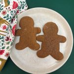 Two einkorn gingerbread men on white plate with holiday print napkin beside