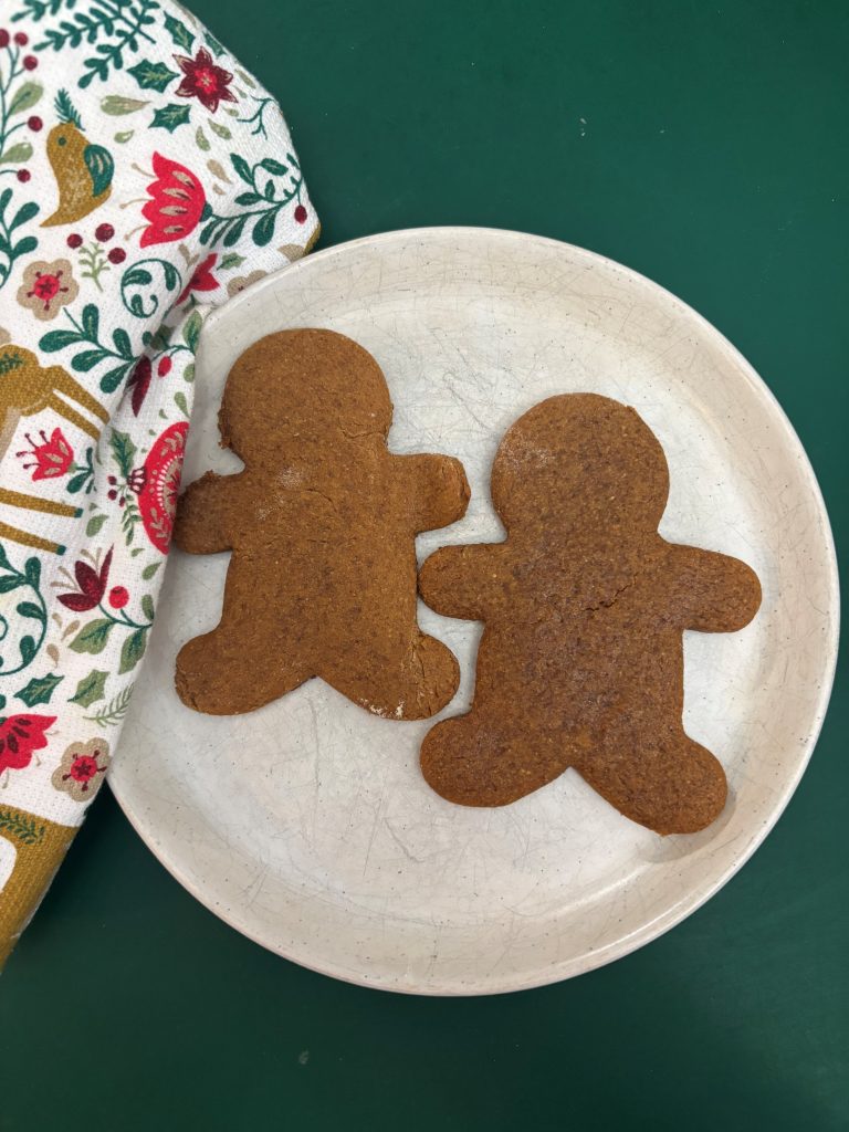 Two einkorn gingerbread men on white plate with holiday print napkin beside