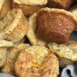 Close up of fresh out of the over cheese and herb muffins in wooden bowl lined with tea towel