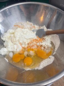 Close up photo of wet and dry ingredients in steel bowl ready to be mixed into Savoury Cheese and Herb Muffins
