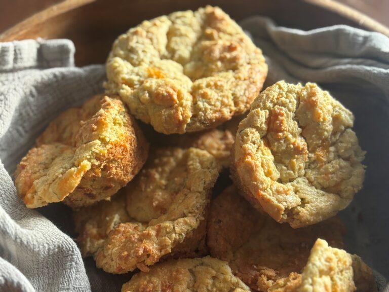 Close up of savoury cheese and herb muffins in wooden bowl lined with grey tea towel