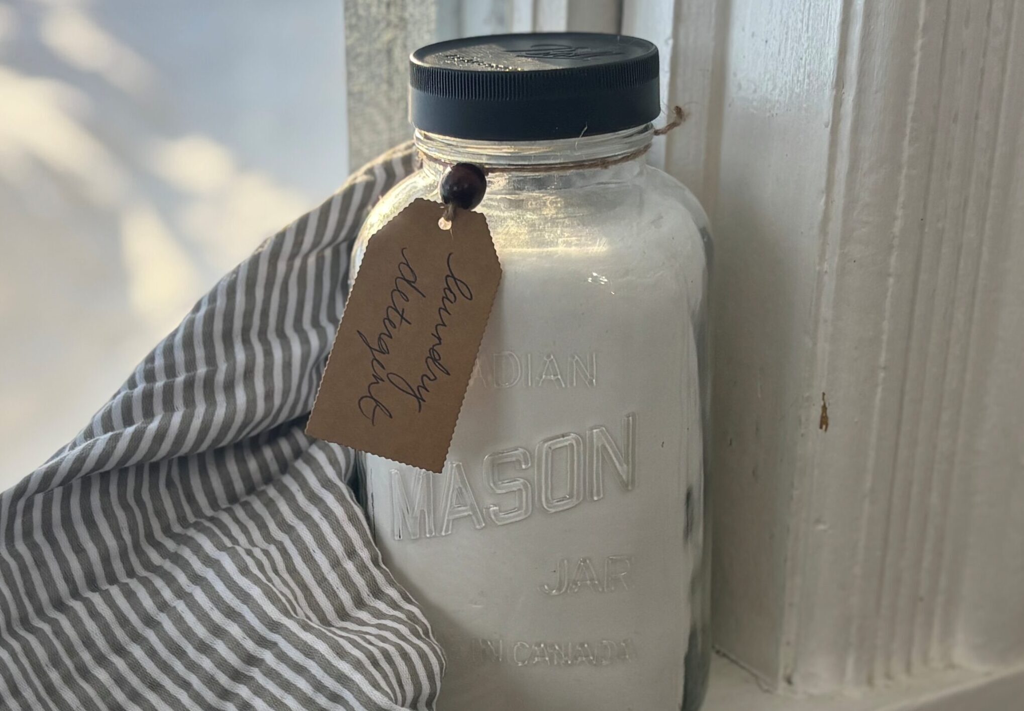 quart sized mason jar on a windowsill filled with homemade powdered laundry detergent