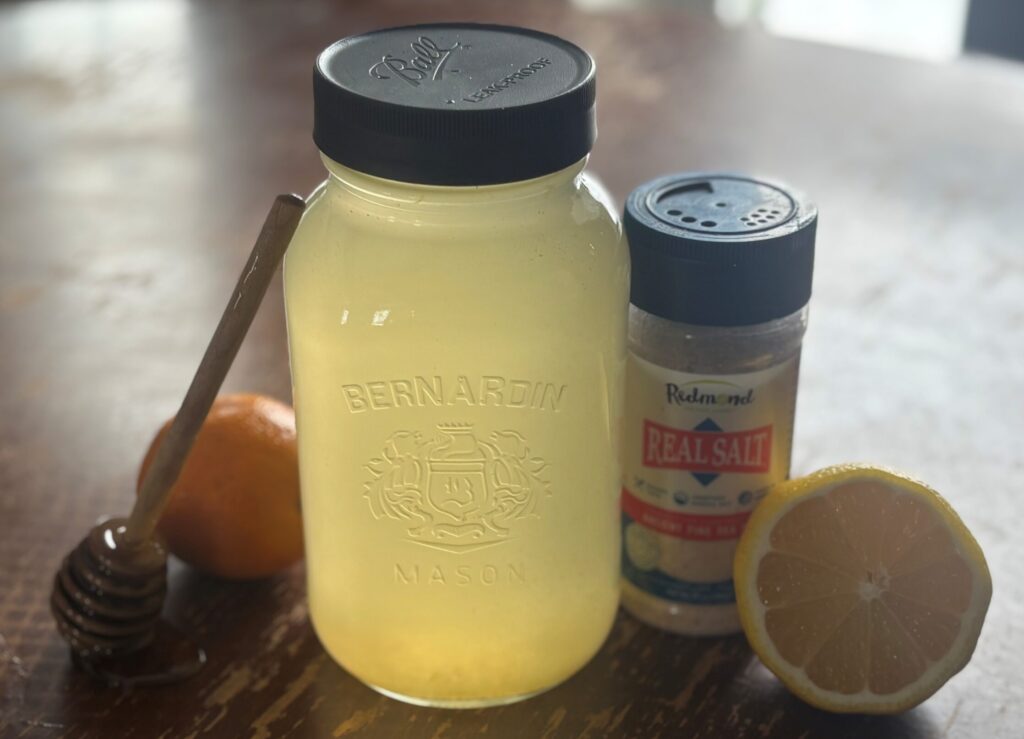 4 cup mason jar on wooden table with lemon, orange, salt and honey stick leaning against jar