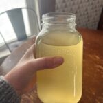 Woman holding jar filled with Homemade electrolyte drink over wooden table