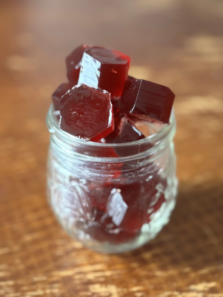 glass jar of deep red homemade gummy candies sitting on wooden table