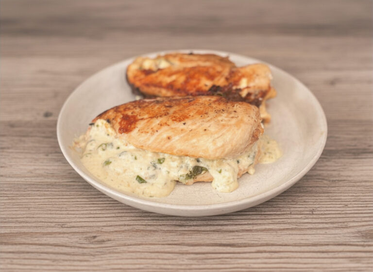 2 stuffed chicken breasts on white plate on light wood countertop