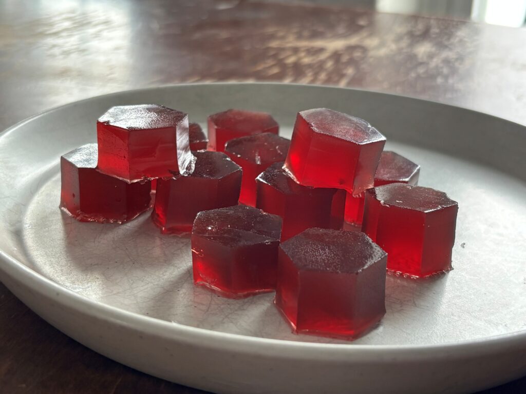 white plate on wooden table containing deep red gelatin gummy candies
