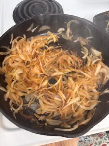 yellow onions sautéing on a stove in a cast iron pan
