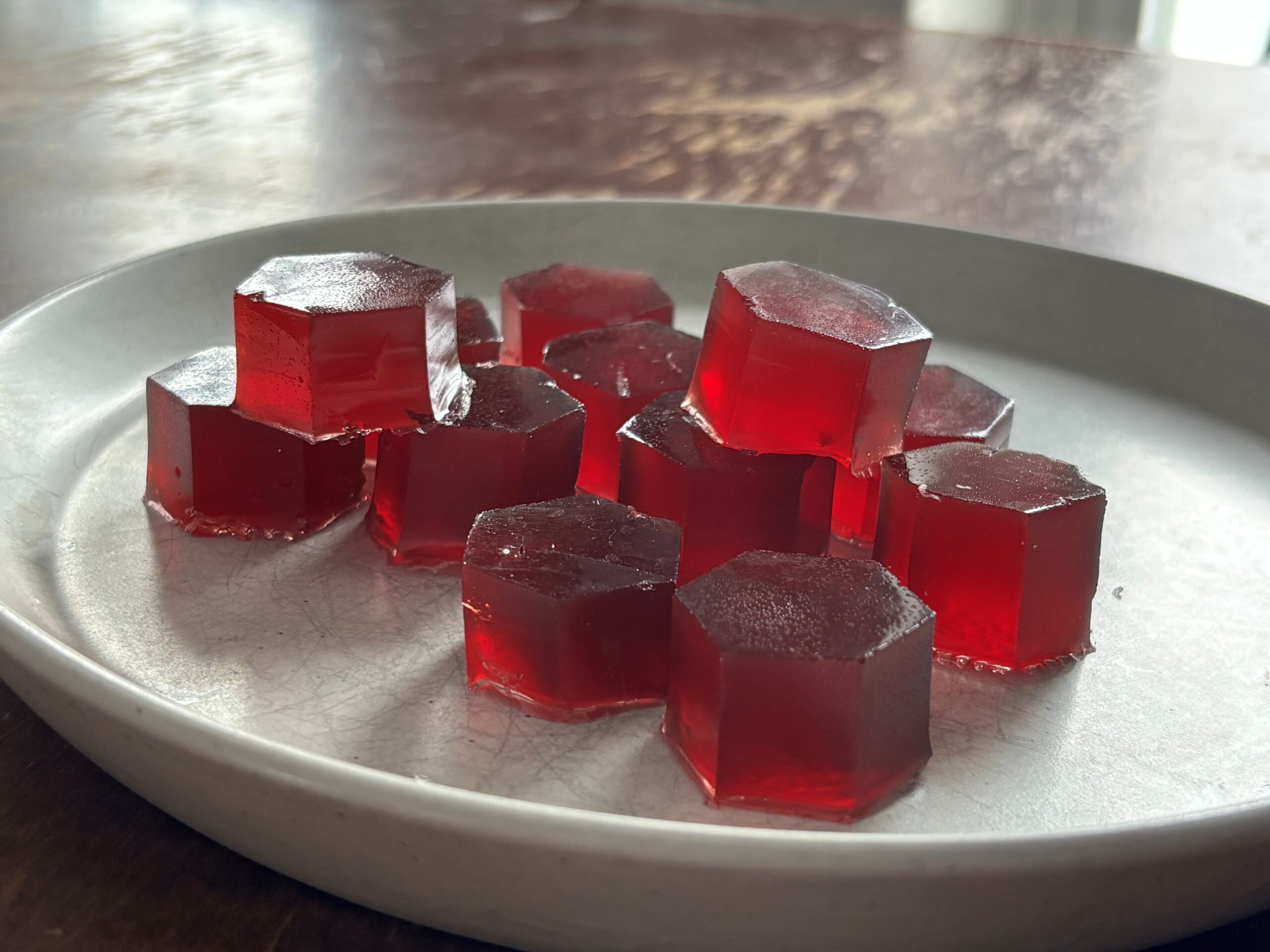 white plate on wooden table containing deep red gelatin gummy candies