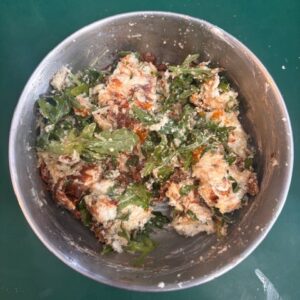 Top view of ingredients for making stuffed chicken filling in large silver bowl on green countertop