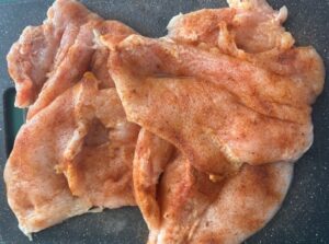 raw, seasoned, and butterflied chicken breast on black cutting board