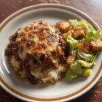 Slow Cooker French Onion Pot roast on mashed potatoes with a side Caesar salad, sitting on dark wooden table and retro plate