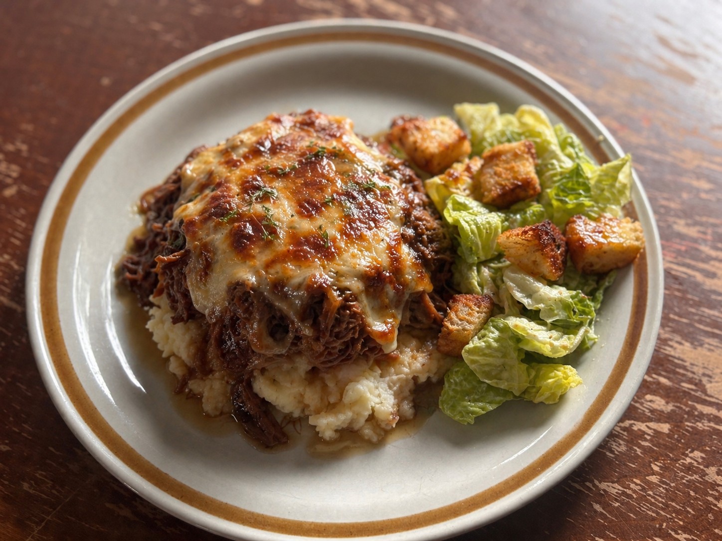 Slow Cooker French Onion Pot roast on mashed potatoes with a side Caesar salad, sitting on dark wooden table and retro plate