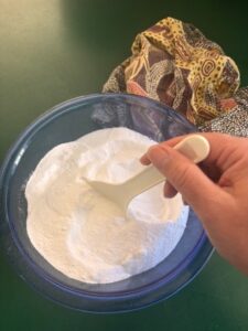 Woman mixing up the ingredients to make a homemade dishwasher powder in blue glass bowl with plastic spoon