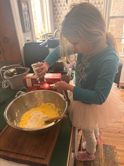 Young girl shaking dried parsley into large bowl of lasagna ingredients in the kitchen.