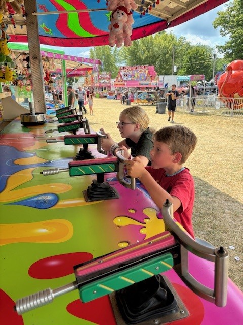 young boy and teen girl at a carnival playing a water gun game at colourful booth