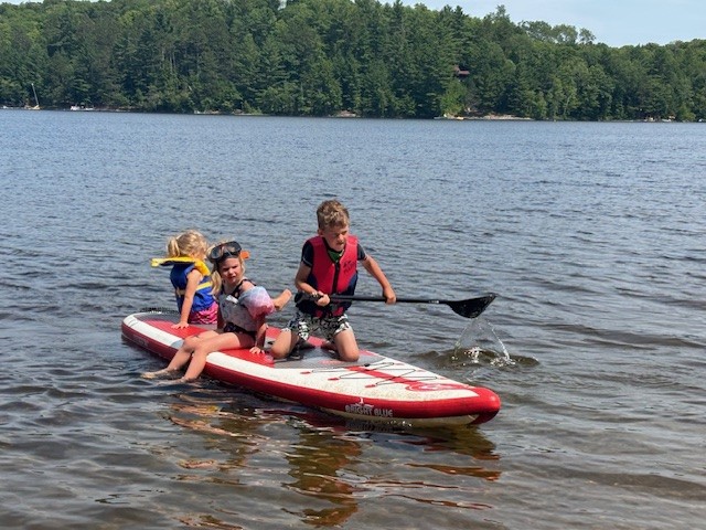 3 children enjoying a paddleboard in a lake on a summer day