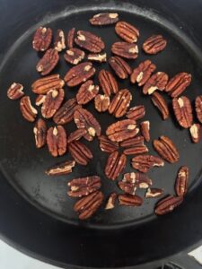 handful of pecans slow roasting on stovetop in black cast iron pan