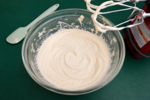 white face cream ingredients whipped in clear glass mixing bowl on green countertop