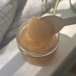 clear glass jar containing gritty light brown sugar scrub with a white background and grey and white tea towel
