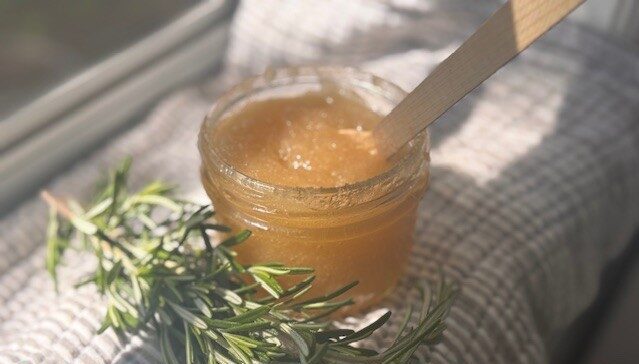 clear glass jar containing sugar scalp scrub sitting on grey and white striped tea towel with wooden spoon in scrub