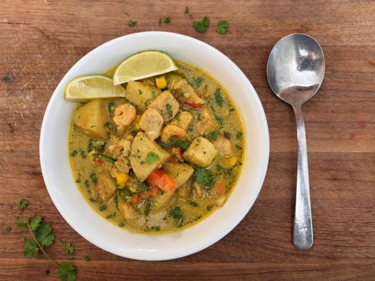 white bowl filled with seafood chowder and fresh parsley, sitting on wood cutting board with silver soup spoon on right side
